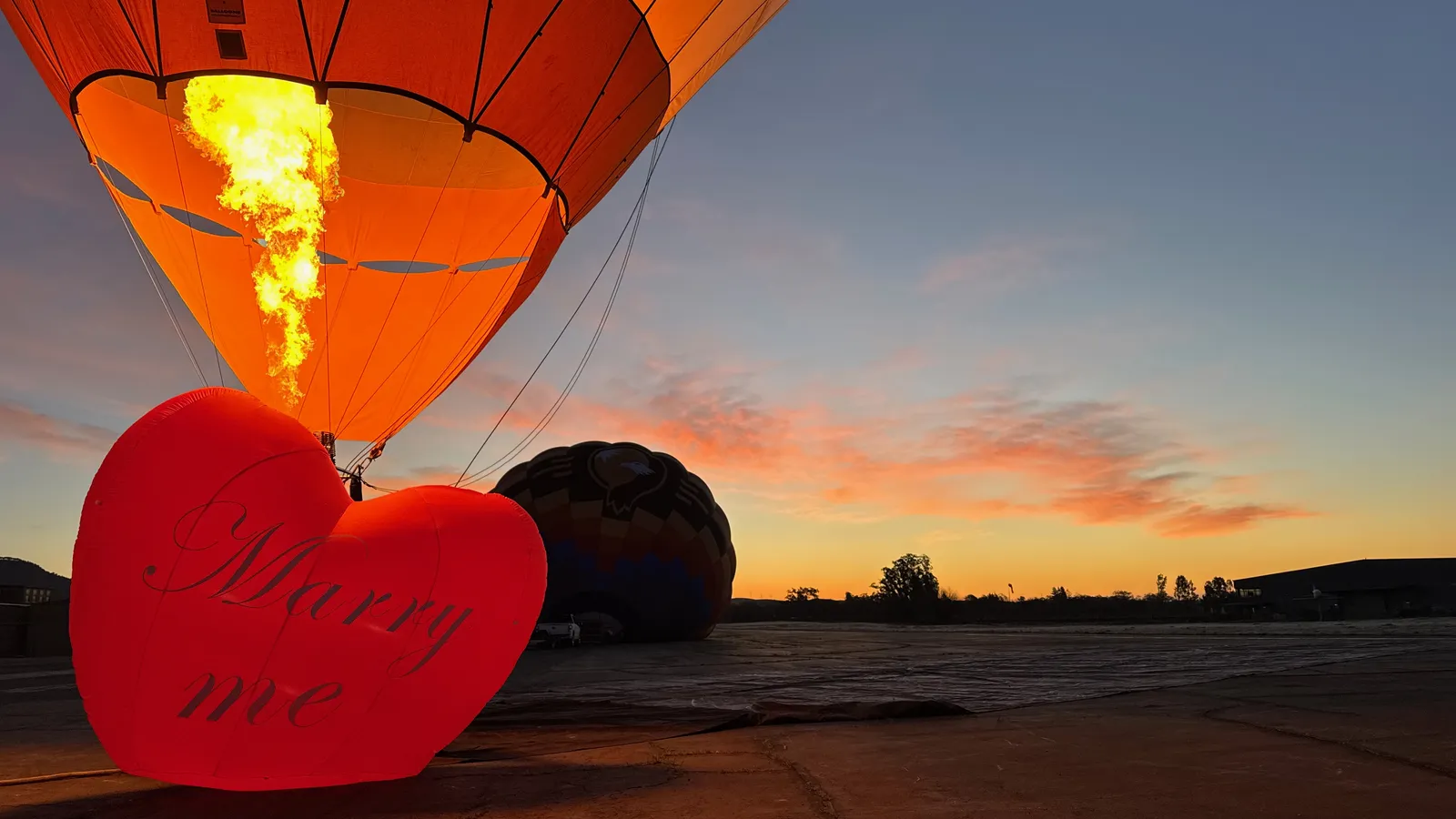 Heart-shaped hot air balloon glowing its burner at dawn