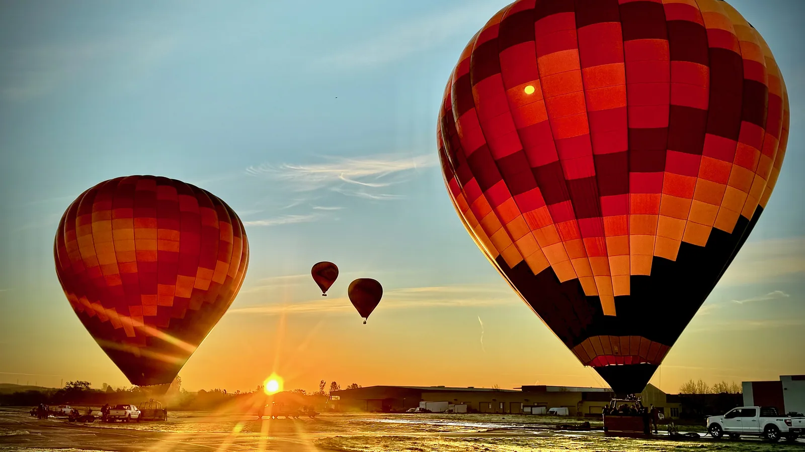 A red hot air balloon canopy glowing against the sunrise over Sonoma wine country