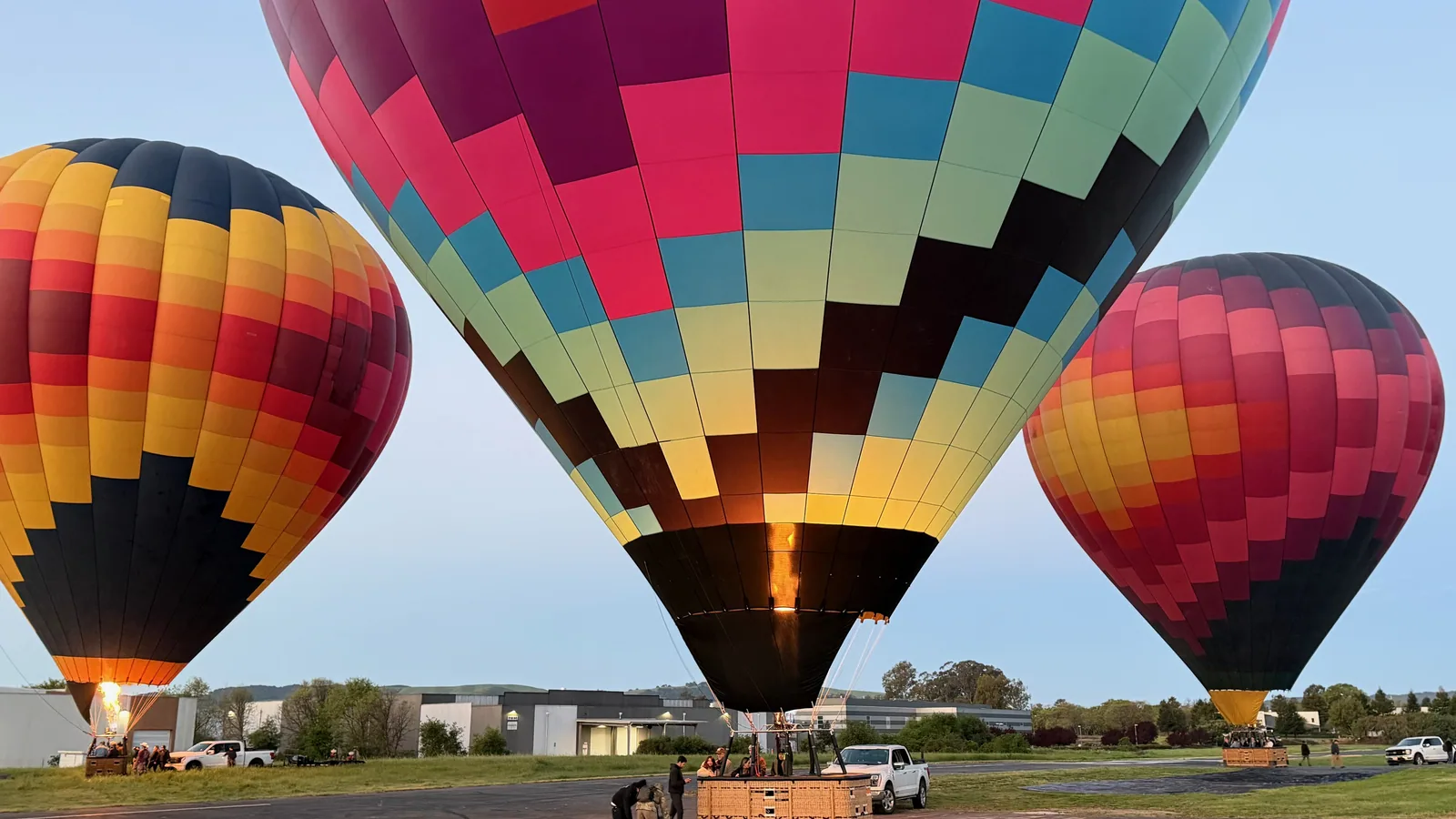 Three colorful Sonoma Ballooning hot air balloons inflated on the airfield at sunrise