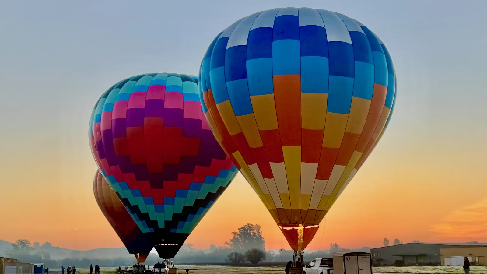 Colorful hot air balloons inflating side by side in the orange glow of sunrise, ready for a group bachelorette flight