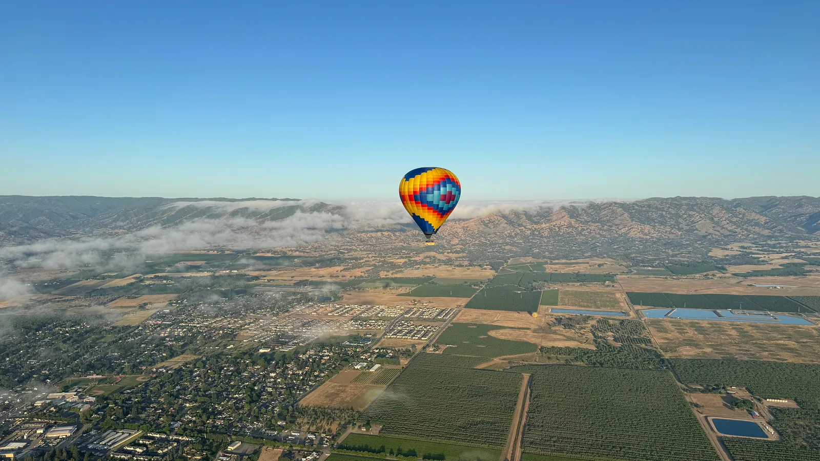 Hot air balloon floating above low morning mist and Sonoma Valley farmland