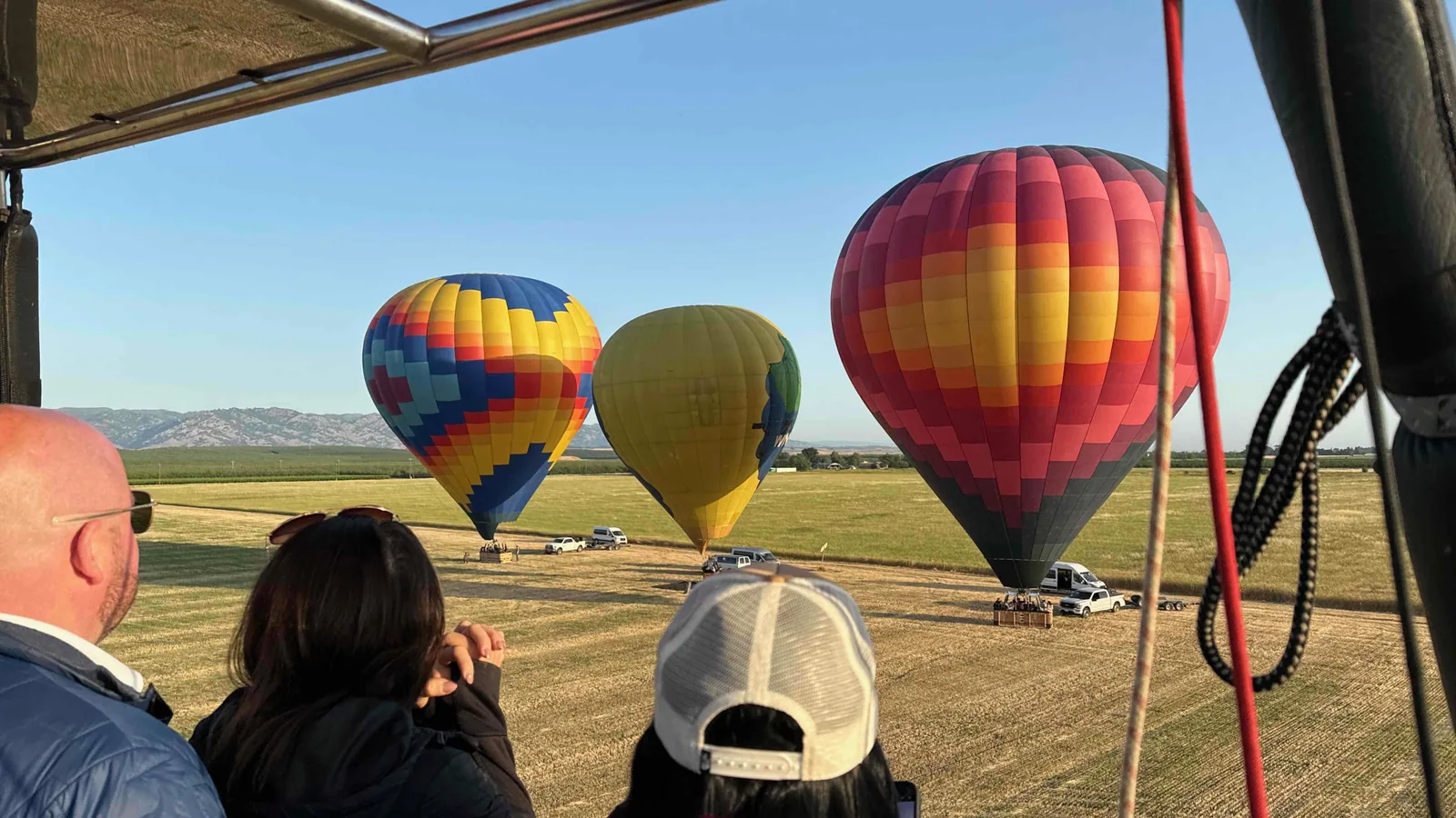 Guests look out from a hot air balloon basket as three balloons stand inflated at sunrise over golden Sonoma fields