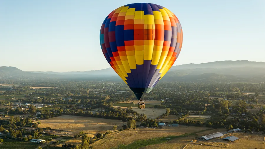Hot air balloon over Sonoma Valley vineyards with hills behind, nearing the end of a flight