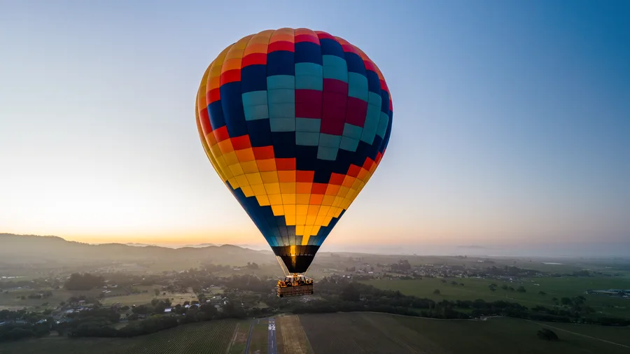 Hot air balloon climbing out over Sonoma Valley in the blue light before sunrise