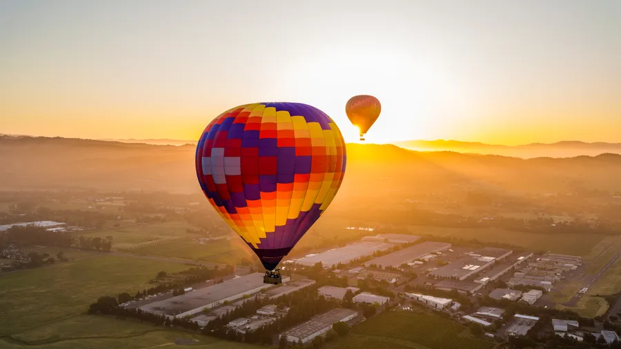 Sun cresting the hills as two hot air balloons drift over Sonoma wine country