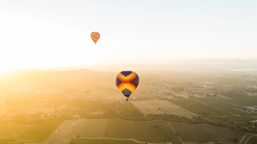 Two hot air balloons drifting through golden morning haze over Sonoma