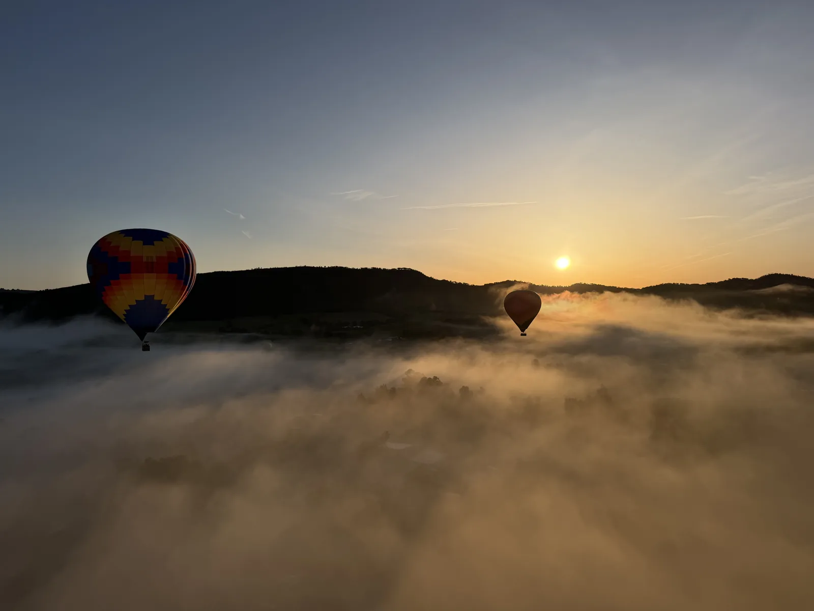 Two hot air balloons drifting above a sea of fog at sunrise over wine country