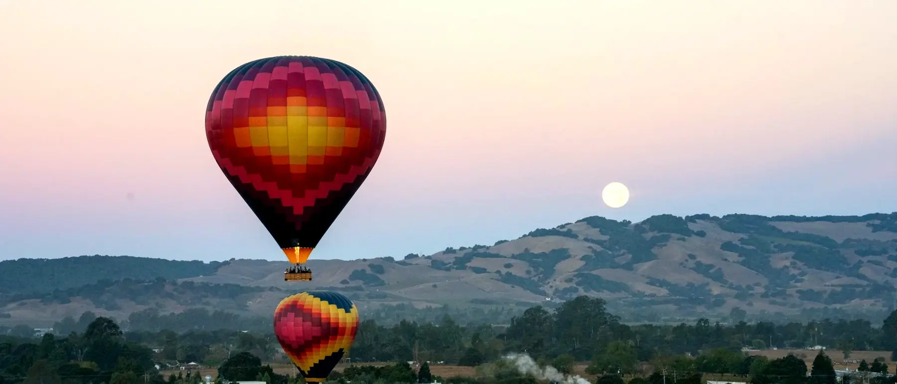 Two balloons over Sonoma Skypark with the moon setting behind the hills
